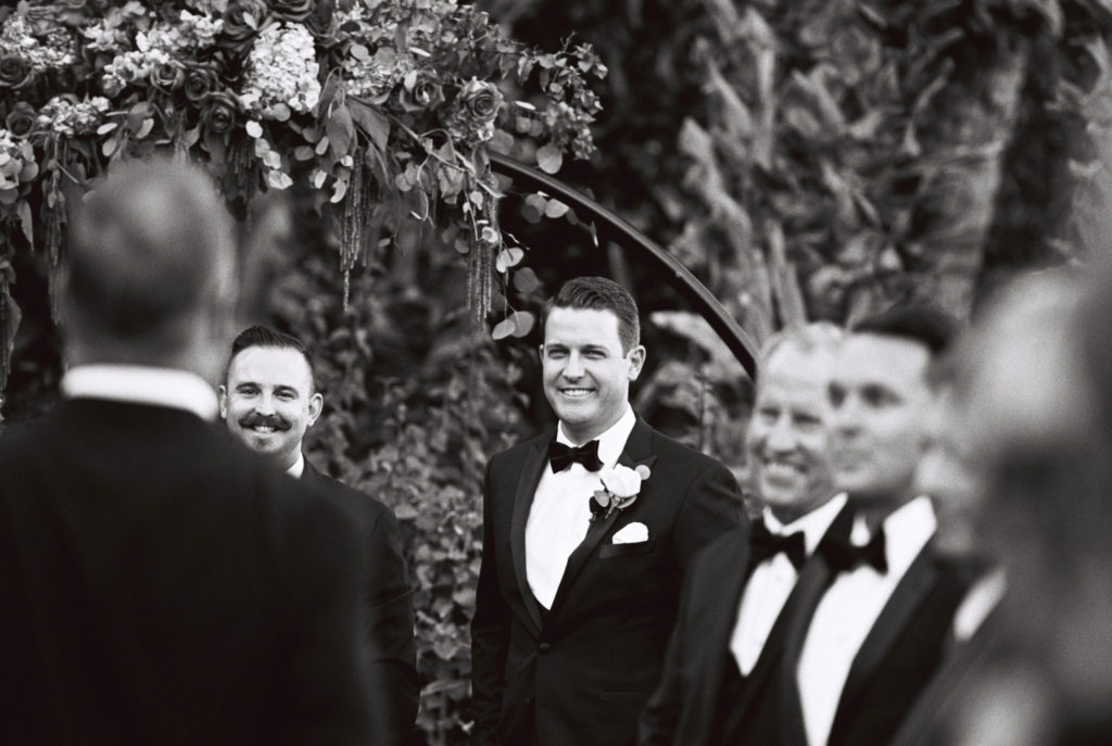 Black and white film image of the groom seeing his bride for the first time as she walks down the aisle

