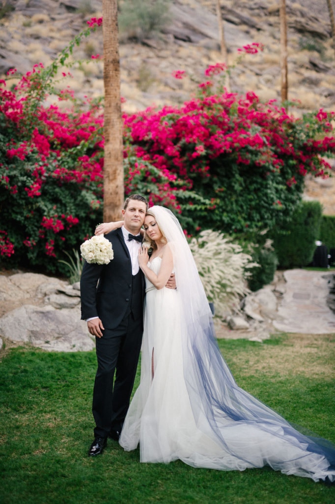 Bride and groom with bougainvillea behind them with bride and her ivory rose bouquet. 