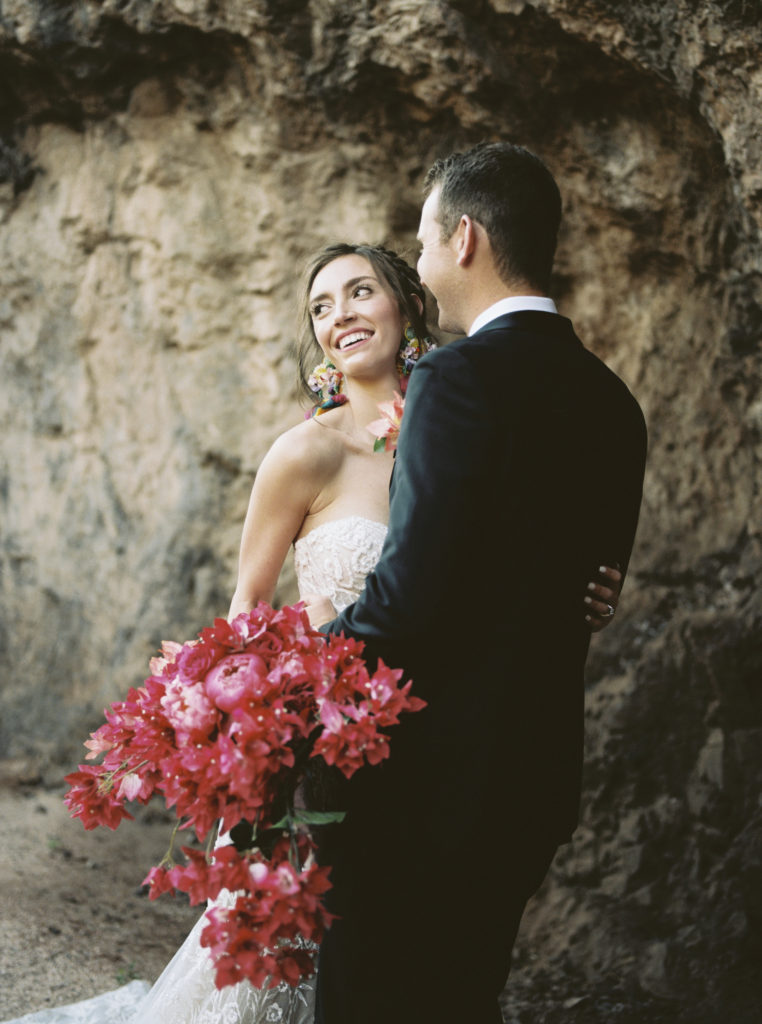 bride and groom in front of rocks with bride holding bougainvillea bouquet