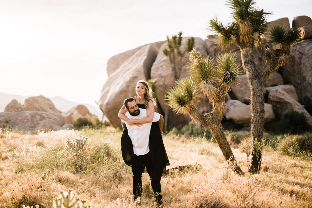 groom holding bride up near boulders for their joshua tree engagement