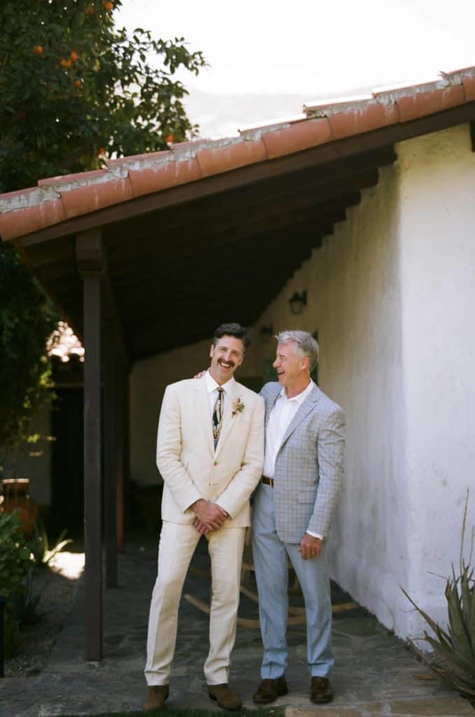 groom laughing with his father in front of an adobe house
