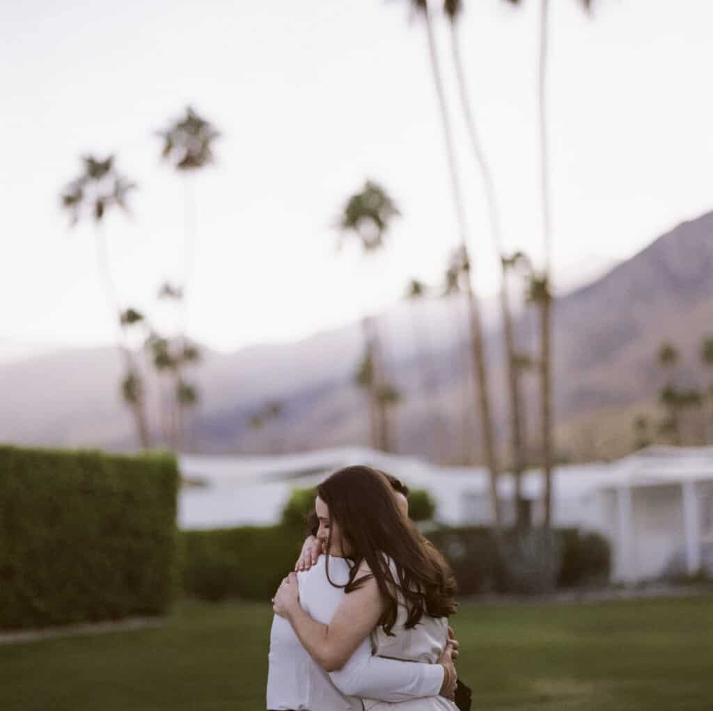 two women hugging on a palm tree lined street in palm springs shot in film